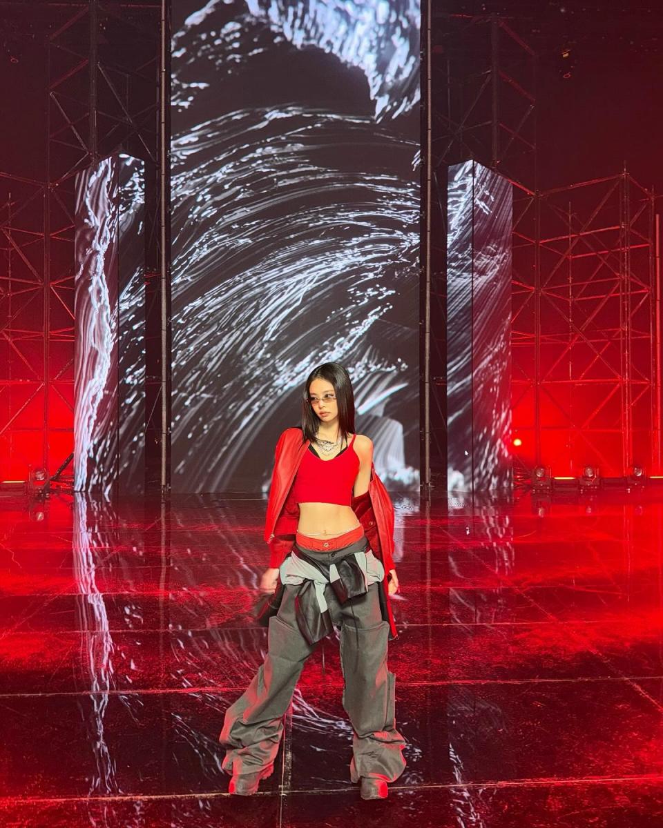 Jennie表演造型示範紅色短版背心搭配超低腰深灰色工裝褲，外搭一件同色系短版皮外套，展現層次感與態度