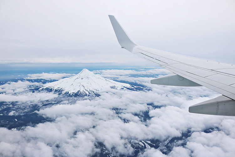 正有一架飛機低空飛過俄勒岡州附近的山上，山間佈滿白雪十分漂亮。